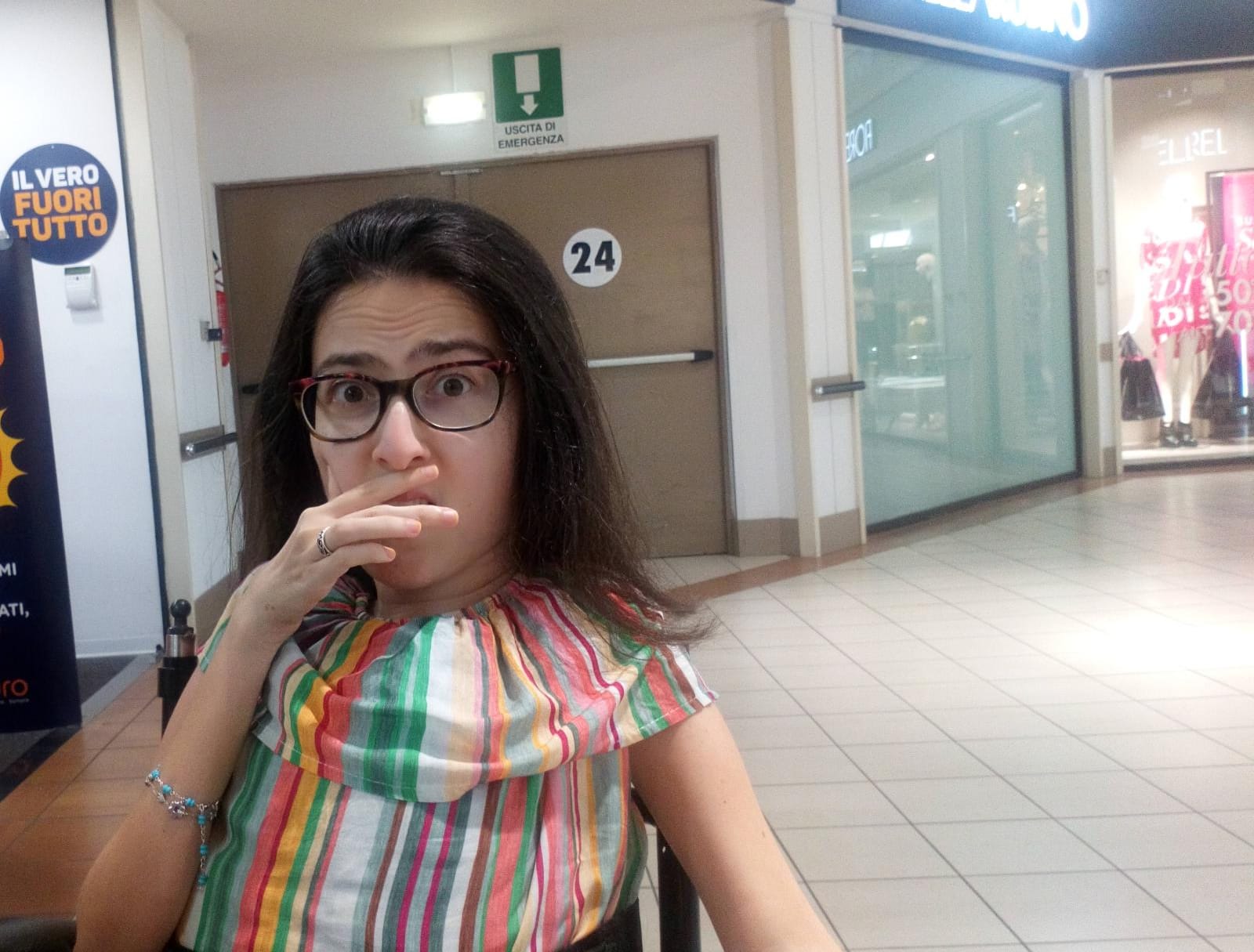 Maria Chiara in un centro commerciale seduta sulla sua sedia con una mano sulla bocca
