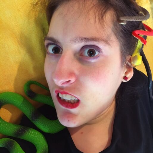 primo piano di Elena vestita da Medusa, con i serpenti finti sulla testa e un'espressione sbigottita e infastidita