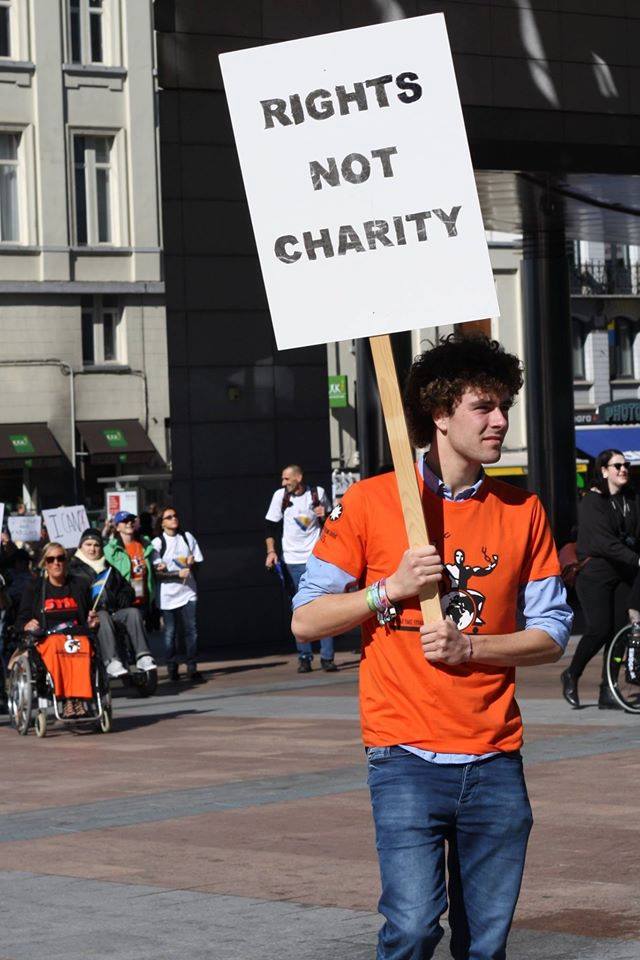 un ragazzo parte di un corteo di dimostranti sfila con un cartello: “Rights not charity”. Indossa la maglietta arancione della Freedom Drive.
