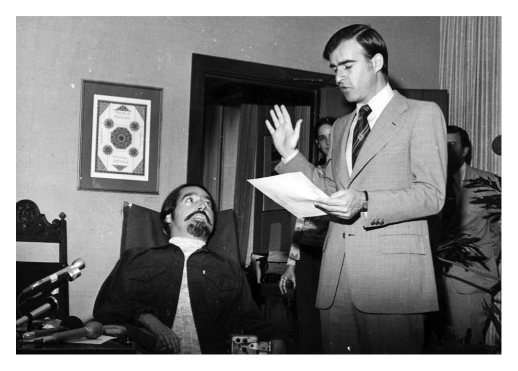 un giovane Ed Roberts guarda il governatore, in giacca e cravatta, che legge da un foglio.